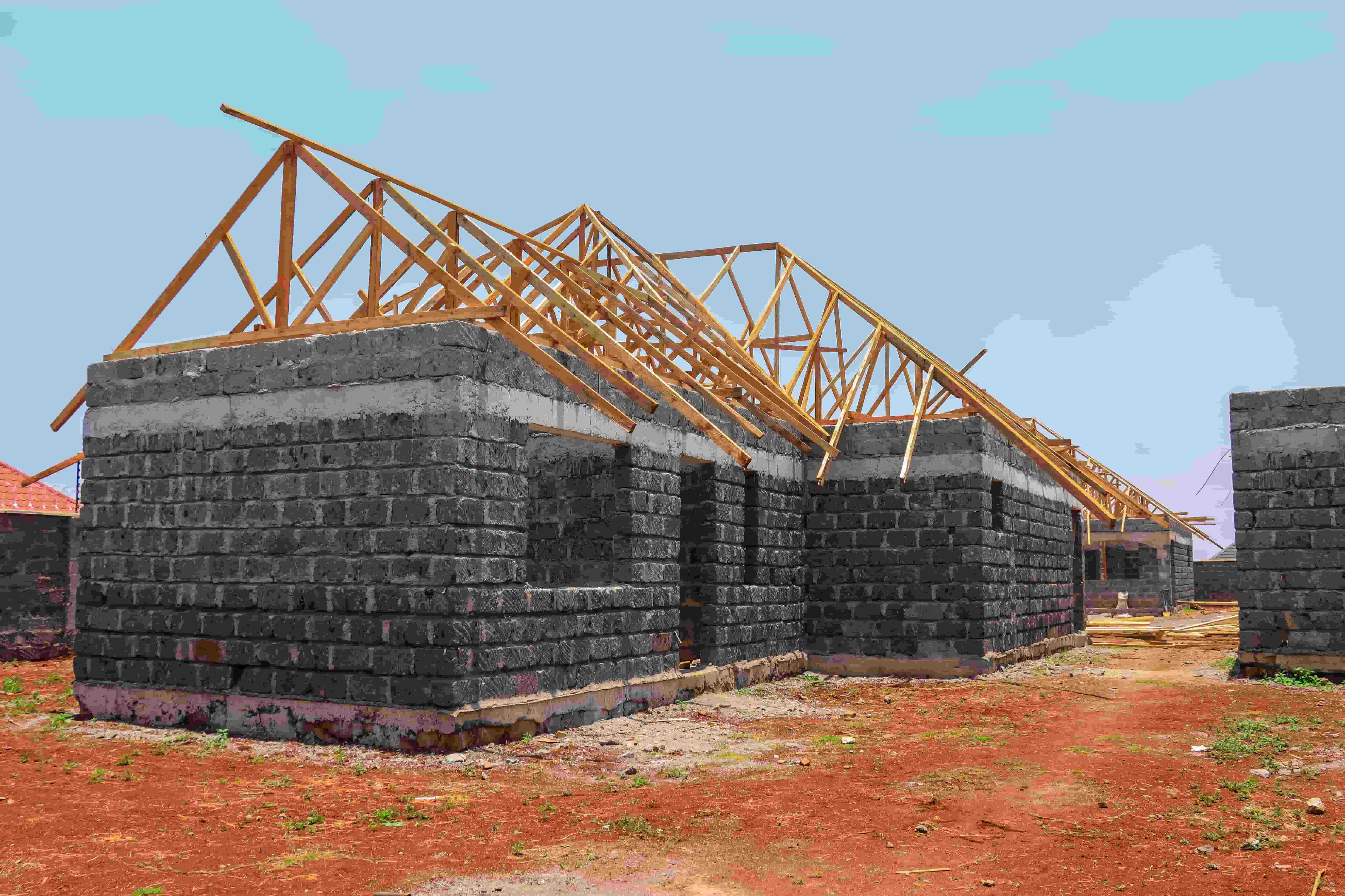 Partially built house with stone walls and wooden roof trusses under construction on a clear day.
