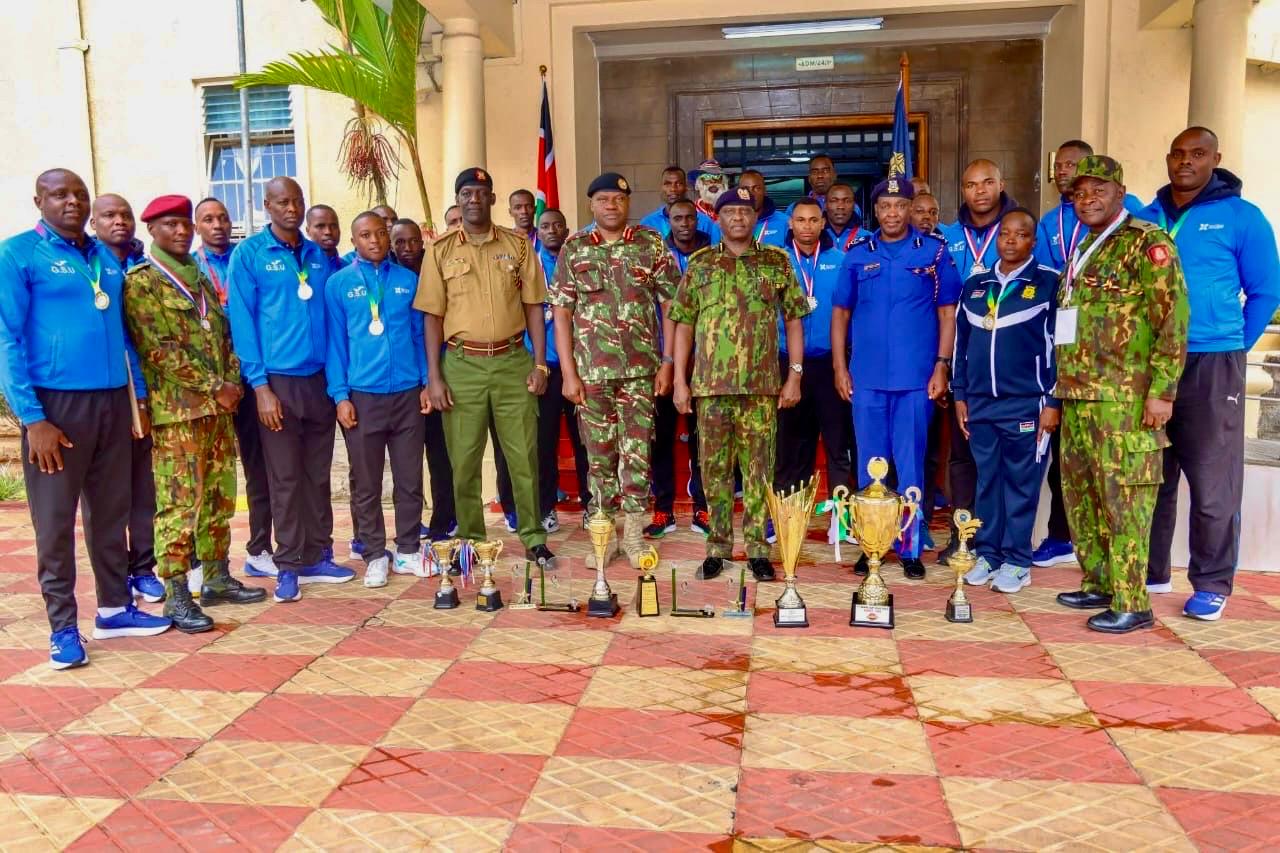 Group photo of officers and athletes in uniform standing behind multiple trophies and medals during the Kenya Cup 2024/2025 award ceremony, with team members wearing blue and camouflage attire.